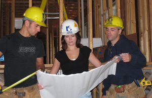 Photo of building construction with woman architect holding blue prints with two male carpenters