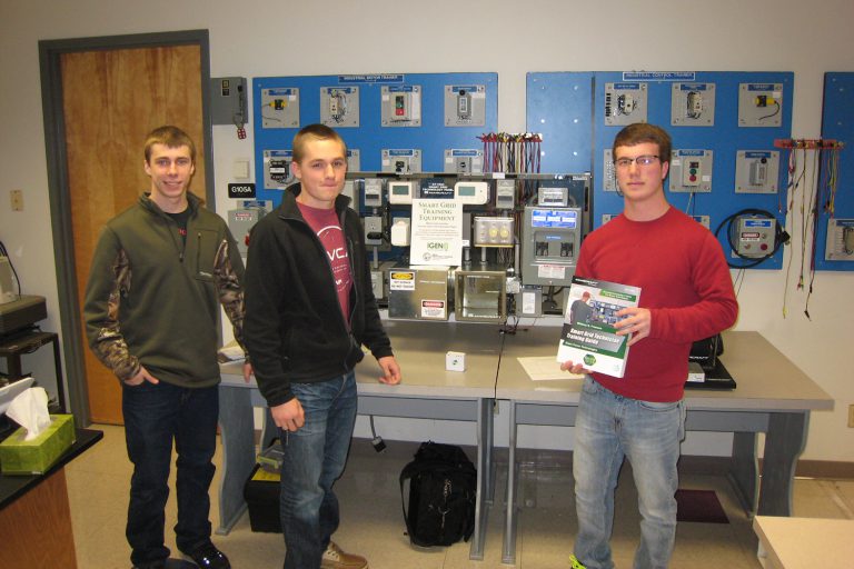 Photo of three male students standing in front of Smart Grid Training Equiment
